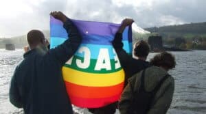 View from behind of protesters holding up a peace flag towards a submarine in the loch