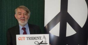Paul Flynn holds a "Cut Trident" poster as he stands beside a CND roller banner