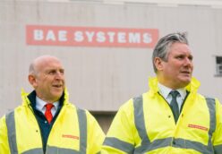 John Healey and and Keir Starmer wear high viz jackets with warehouse in the background with BAE Systems sign