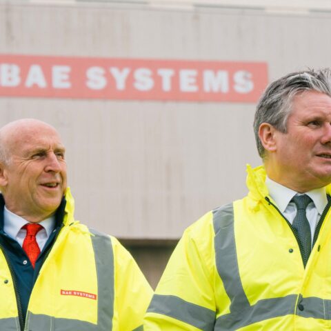 John Healey and and Keir Starmer wear high viz jackets with warehouse in the background with BAE Systems sign