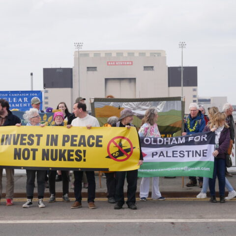 Protesters with banner stand on bridge in front of BAE Shipyard, Barrow.