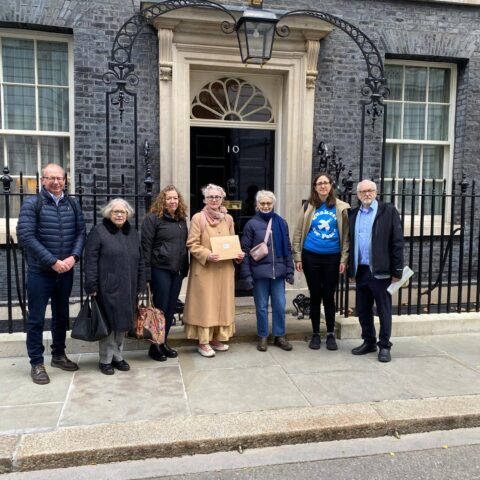 A group of people holding a letter stand outside No.10 Downing Street. From left to right: Andrew Jackson, Pax Christi; Lindsey German, Stop the War Coalition; Fran Heathcote, PCS; Sophie Bolt, CND; Victoria Brittain; Grace Da Costa, Quakers in Britain; Jeremy Corbyn MP